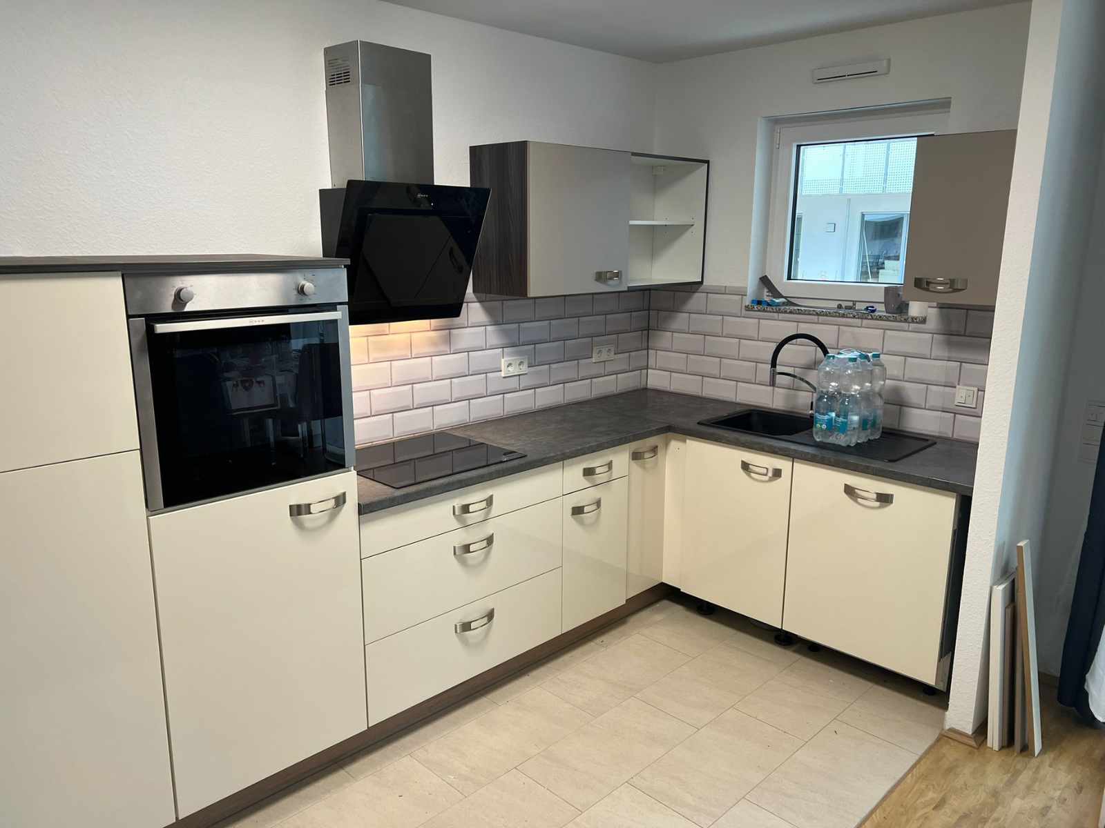 Eine neu montierte Eck - Küche und weiß mit dunkler Arbeitsplatte. Wandschränke neben dem Fenster in weiß und eine schwarze Abzugshaube.