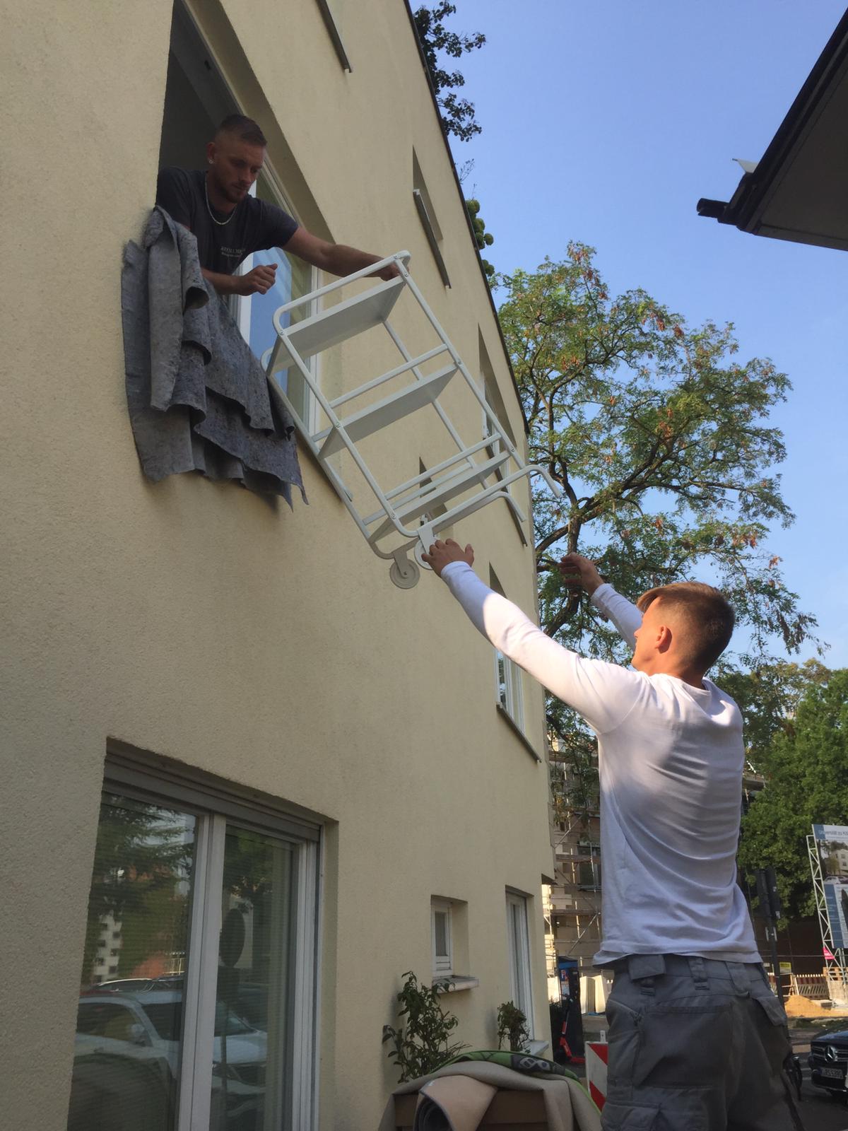 Wohnungsauflösung Köln: Reuter Umzüge gibt vollen Körpereinsatz. Ein Mitarbeiter übergibt über ein Fenster ein Möbelstück an seinen Kollegen. 