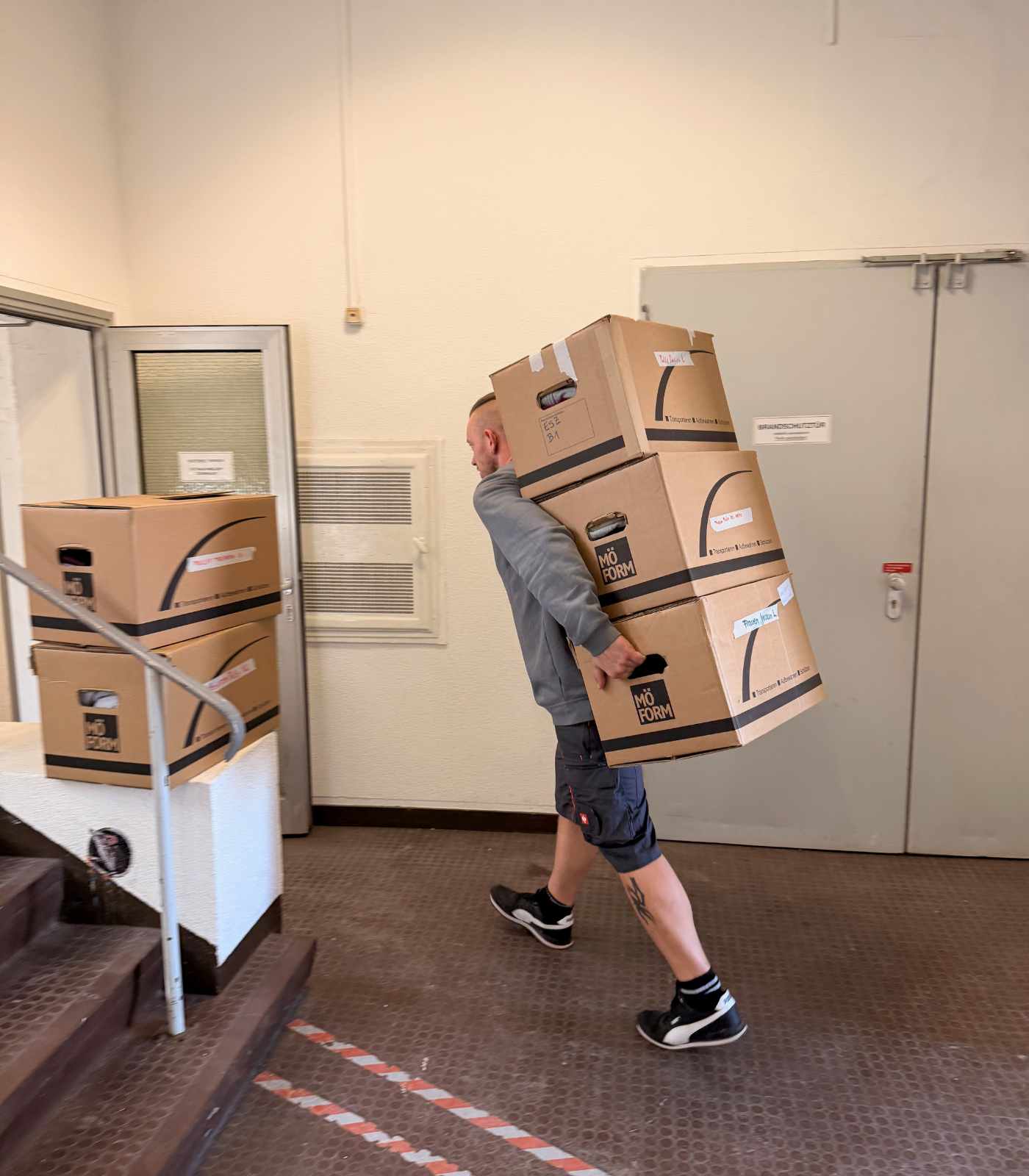 Ein Mitarbeiter von Reuter Umzüge trägt mehrere beschriftete Umzugskartons durch einen Eingangsbereich.