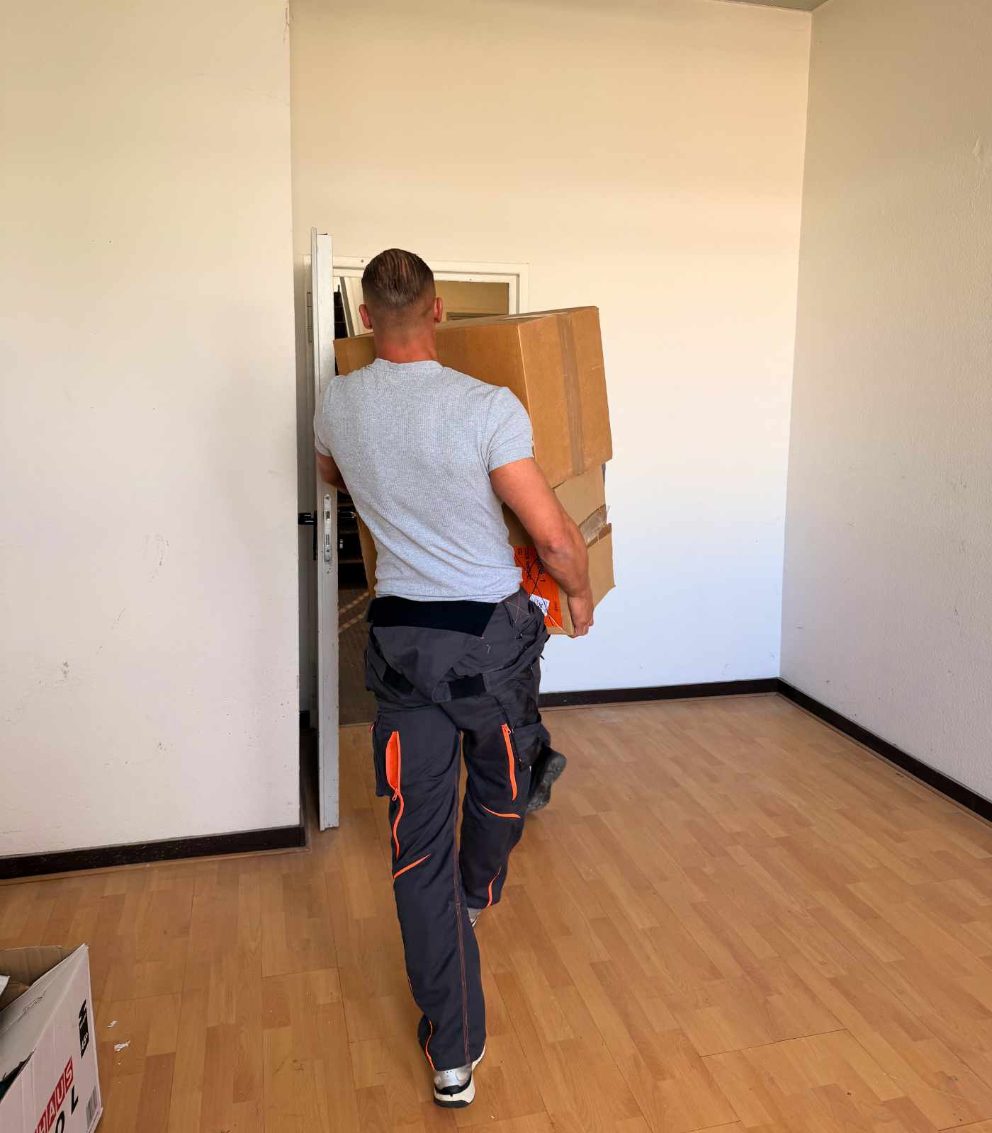 Ein Mitarbeiter von Reuter Umzüge trägt mehrere Umzugskartons durch einen leeren Büroraum.