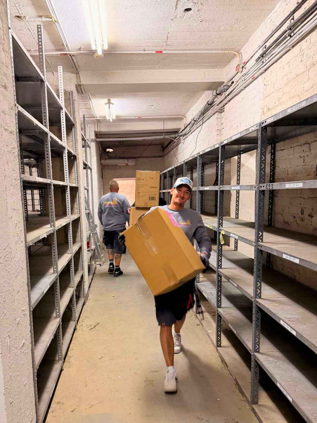 Ein Mitarbeiter von Reuter Umzüge transportiert Kartons durch einen Lagerraum mit Regalsystemen. Das Umzugsunternehmen Köln übernimmt auch Lager- und Firmenumzüge zuverlässig.